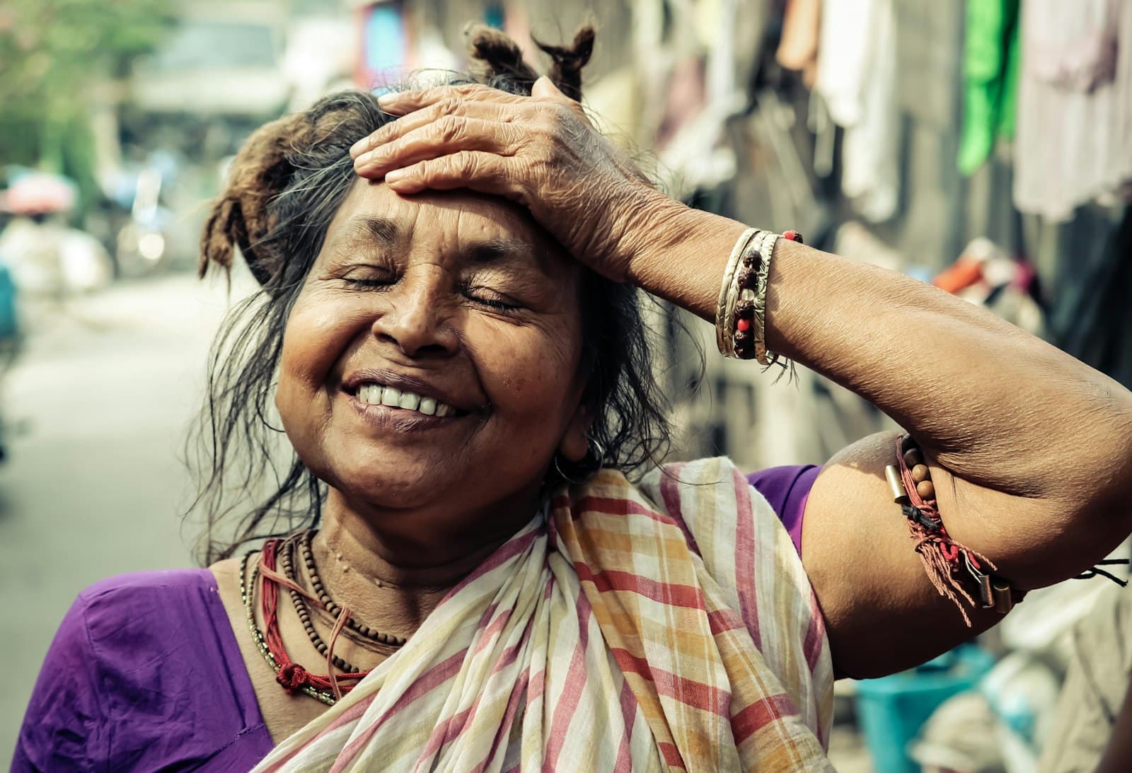 A woman laughing, hand to her forehead, on a street in India